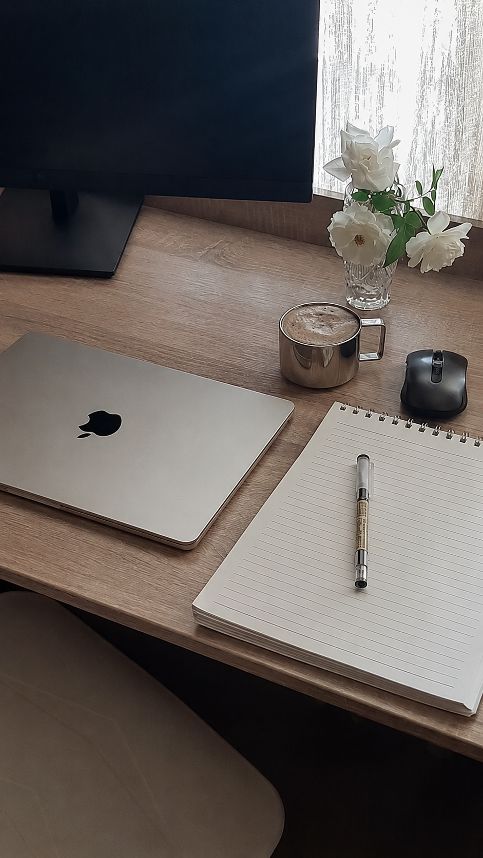 Mesa de trabalho com notebook, caderno, caneta, xícara de café e flores brancas